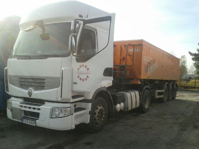 Biała ciężarówka Renault z pomarańczową naczepą MEGA, zaparkowana na placu, z widocznym logo HOYER GROUP na kabinie.