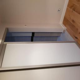 Eurodis Sp.zoo - Szklana ściana działowa z przesuwnymi drzwiami w łazience, widoczna z dołu, z drewnianą podłogą w tle.