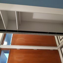 Eurodis Sp.zoo - Wnętrze szafy wnękowej z przesuwnymi drzwiami lustrzanymi, widok z dołu na półki i system mocowań, odbicie drzwi w lustrze.