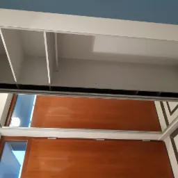 Wnętrze szafy wnękowej z przesuwnymi drzwiami lustrzanymi, widok z dołu na półki i system mocowań, odbicie drzwi w lustrze.