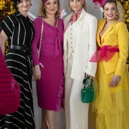 Cztery kobiety w eleganckich kreacjach i kapeluszach, pozujące na tle błyszczącej ściany i balon&oacute;w, z widocznym logo 'Atmosfera' w tle.