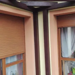 Drewniana konstrukcja z belek nad oknami z roletami zewnętrznymi, widok z dołu na zewnątrz budynku.