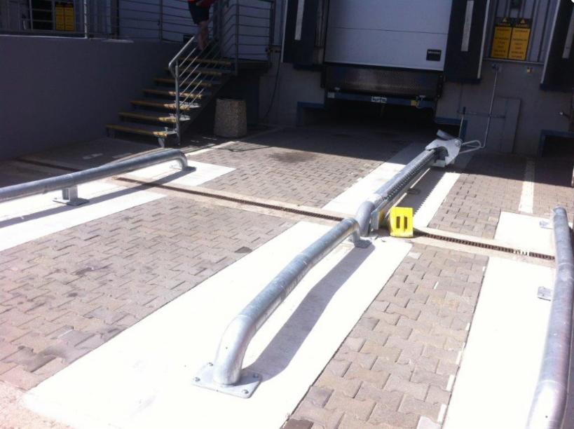 Rampa załadunkowa z zabezpieczeniami w postaci metalowych barier, widoczne kostki brukowe i fragment schodów.