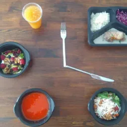 Kompozycja z czterech dań w czarnych pojemnikach: sałatka z owocami i orzechami, zupa pomidorowa, sałatka z makaronem i serem, danie mięsne z ryżem i surówką, uzupełniona sokiem pomarańczowym...