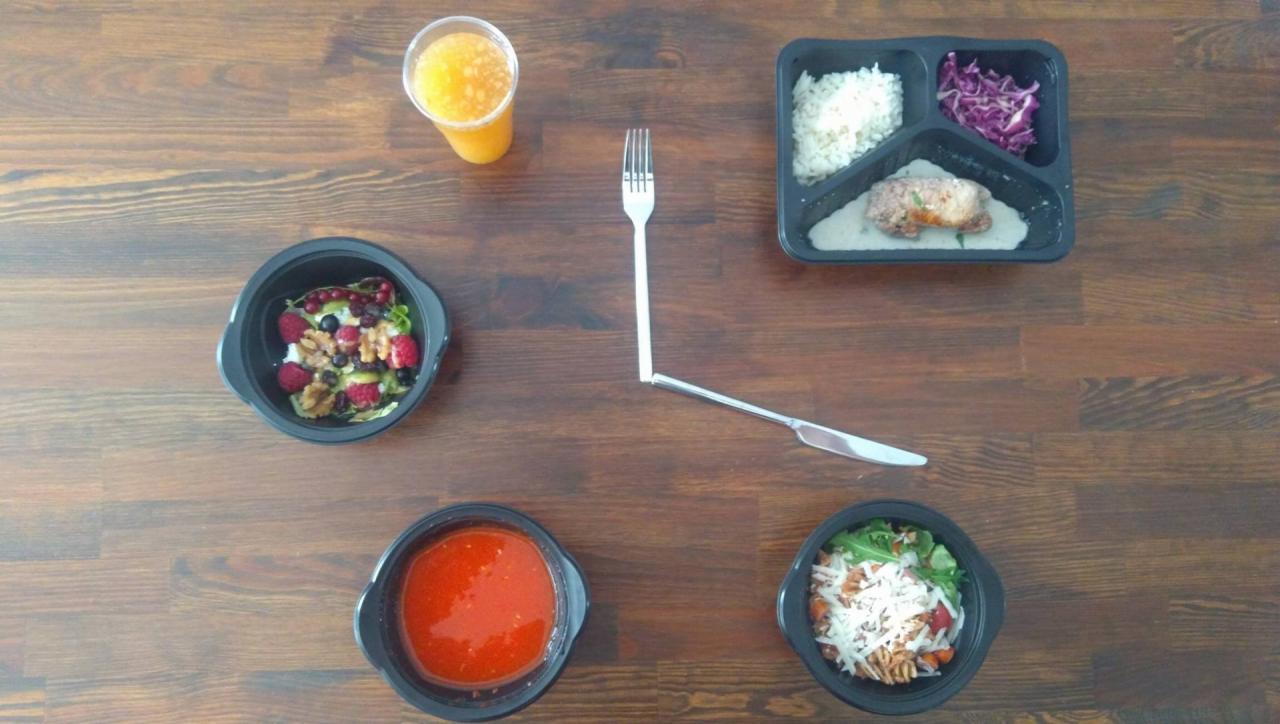 Kompozycja z czterech dań w czarnych pojemnikach: sałatka z owocami i orzechami, zupa pomidorowa, sałatka z makaronem i serem, danie mięsne z ryżem i surówką, uzupełniona sokiem pomarańczowym...