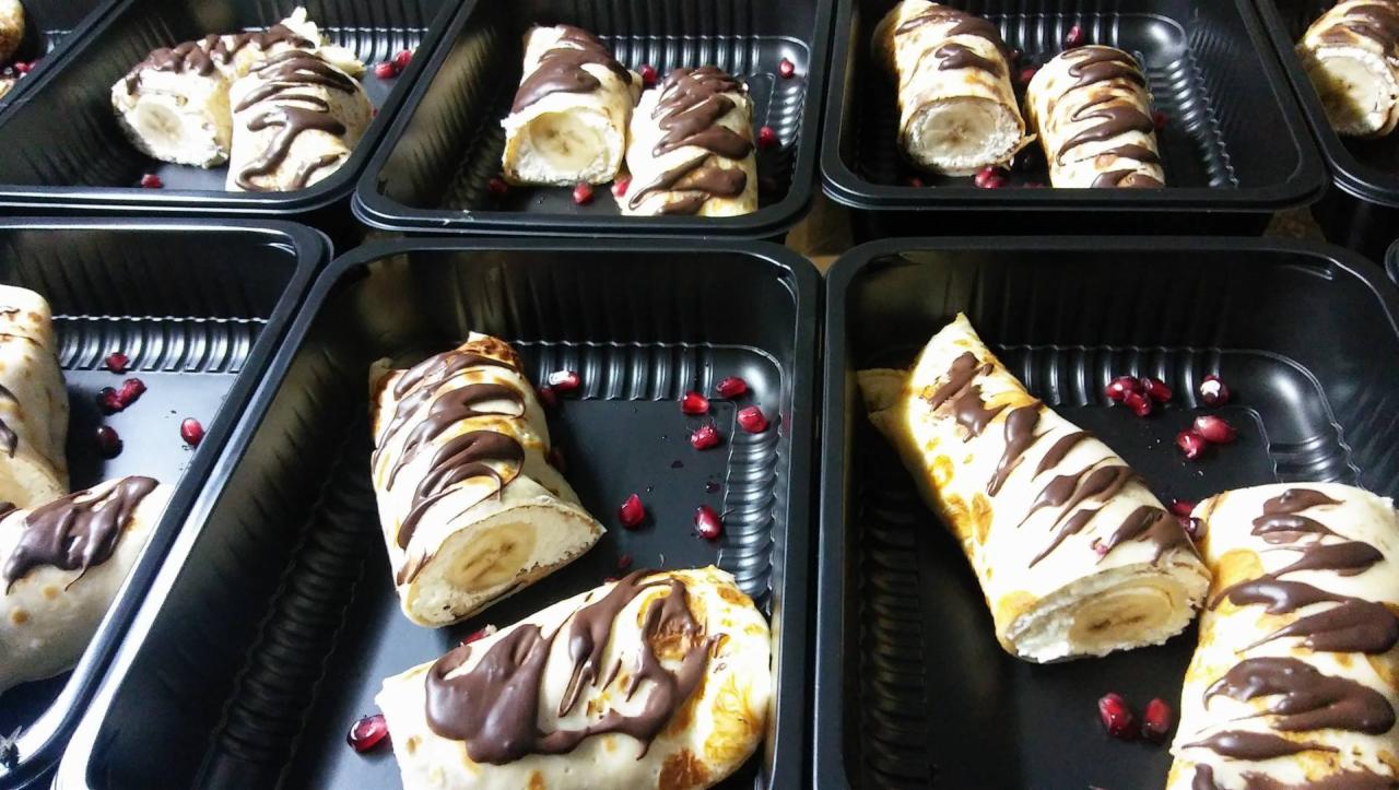 Naleśniki z bananem i polewą czekoladową ułożone w czarnych tackach, ozdobione granatem.