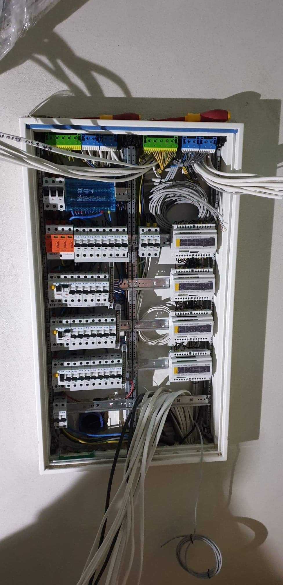 Rozdzielnia elektryczna w trakcie montażu, widoczne przewody, bezpieczniki, ograniczniki przepięć, listwy zaciskowe i narzędzie - śrubokręt leżący na górze.