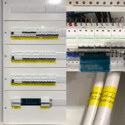 Rozdzielnica elektryczna z bezpiecznikami różnicowoprądowymi i głównym, okablowanie z oznaczeniami, widok z bliska na elementy instalacji elektrycznej.