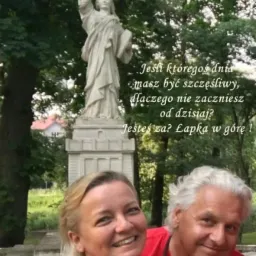 Uśmiechnięta para na tle pomnika Statuy Wolności z sentencją o szczęściu i adresem strony internetowej w dolnej części kadru.