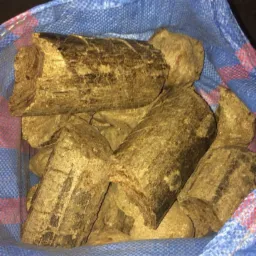 Cylindryczne kawałki opału w niebieskim worku z tworzywa sztucznego, widoczne ślady brudu i drobne pęknięcia na powierzchni.