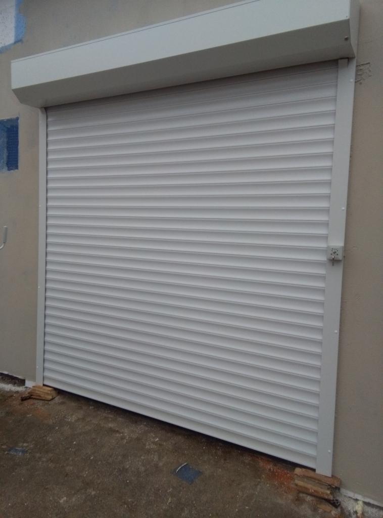 Zewnętrzna, biała roleta antywłamaniowa zamontowana na ścianie budynku, widoczny zamek na boku.