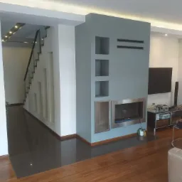 Nowoczesny salon z kominkiem w zabudowie, podłoga z parkietu i płytek, schody z szklaną balustradą w tle, oświetlenie LED.