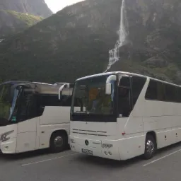 Dwa białe autokary Mercedes parkują na tle górskiego krajobrazu z wodospadem w Norwegii, widoczny numer rejestracyjny LU 476GY.