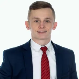 Portret uśmiechniętego młodego mężczyzny w granatowym garniturze i czerwonym krawacie w paski na białym tle.