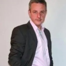 Portret mężczyzny w ciemnej marynarce i jasnej koszuli, na jasnym tle.