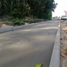 Przygotowany podkład pod chodnik z ułożonymi obrzeżami betonowymi, widok z perspektywy pieszego, w tle zieleń i budynki.