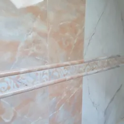 Wykończona ściana łazienki z marmurowymi płytkami w odcieniach beżu i bieli, z dekoracyjnym pasem płytek z ornamentem kwiatowym.