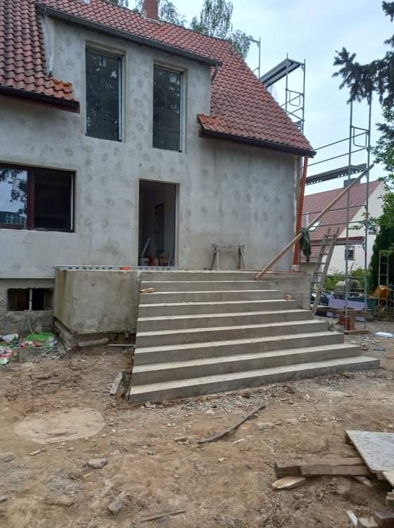 Dom w trakcie remontu w Częstochowie: widoczne nowe betonowe schody wejściowe, otynkowana elewacja z przygotowanymi otworami okiennymi i drzwiami, rusztowania z boku budynku.