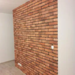 Ściana akcentowa z cegły klinkierowej w nowoczesnym wnętrzu, widoczny włącznik światła i gniazdko elektryczne.