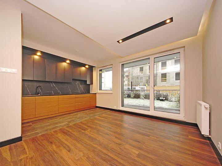 Nowoczesna kuchnia z drewnianymi szafkami dolnymi i ciemnoszarymi górnymi, marmurowy backsplash, parkiet i duże okno przesuwne z widokiem na ogród w tle.