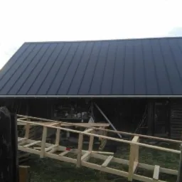 Nowe, grafitowe pokrycie dachowe z blachy trapezowej na drewnianym budynku gospodarczym, widoczne rusztowanie z surowego drewna.