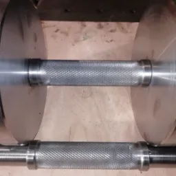 Metalowa sztanga z radełkowanym uchwytem, leżąca na drewnianej powierzchni.