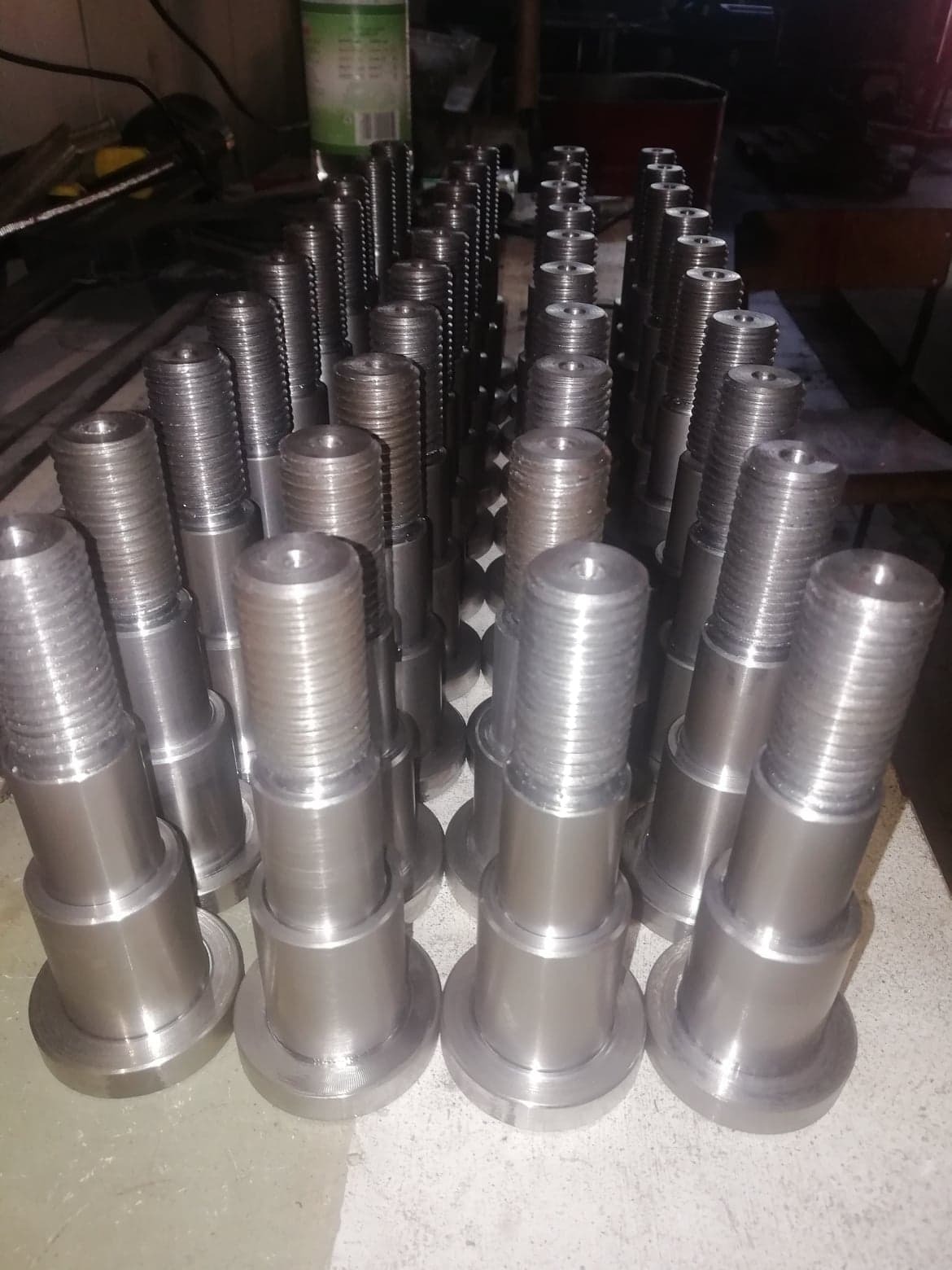 Partia obrobionych metalowych śrub z gwintem, ułożonych rzędami na stole warsztatowym, widoczne ślady obróbki.