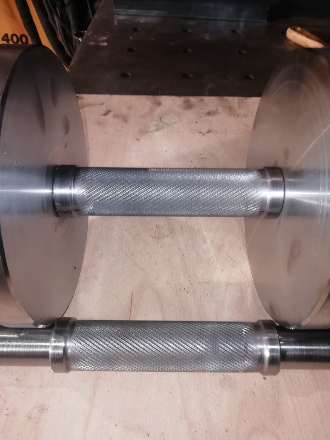 Metalowa sztanga z radełkowanym uchwytem, leżąca na drewnianej powierzchni.