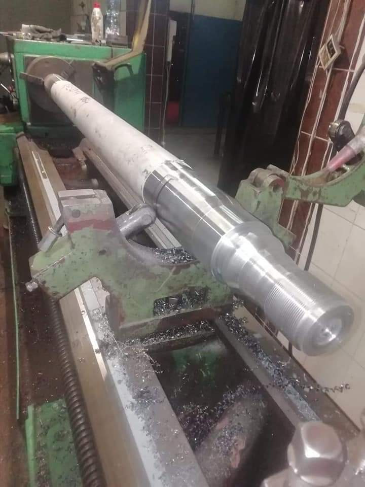 Obrabiany metalowy wał w tokarce; widoczne wióry i fragmenty narzędzia skrawającego.