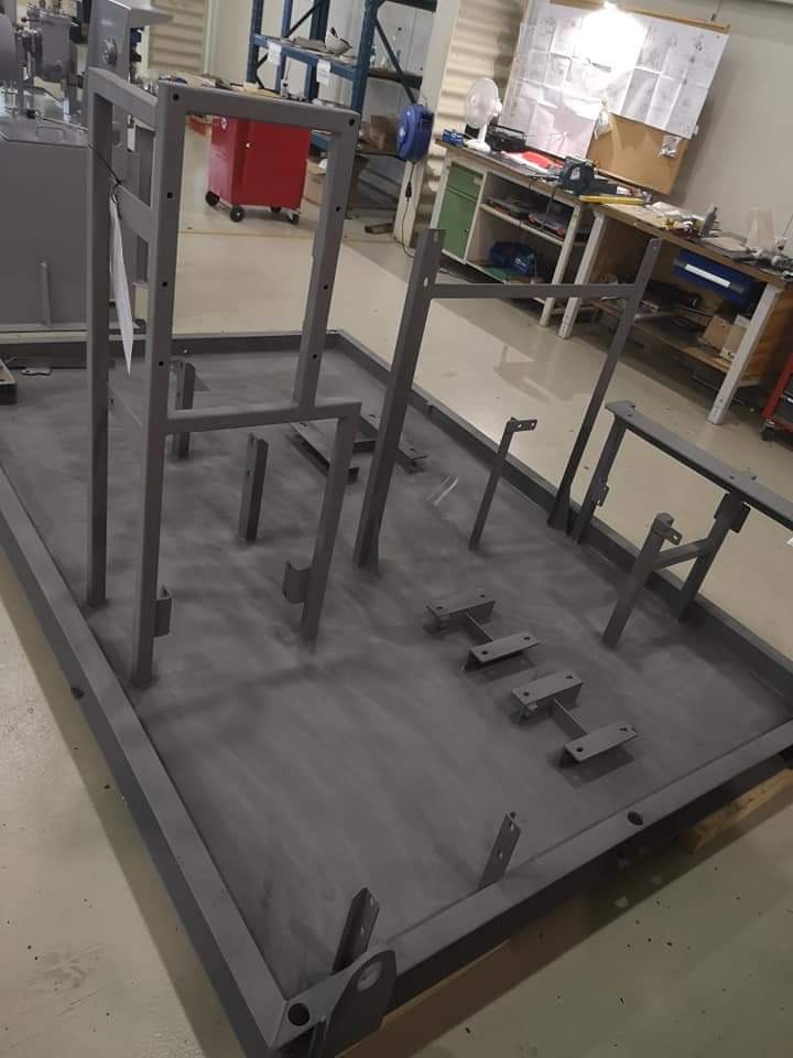 Metalowa konstrukcja spawana, pomalowana na szaro, w warsztacie, z widocznymi elementami montażowymi i otworami.