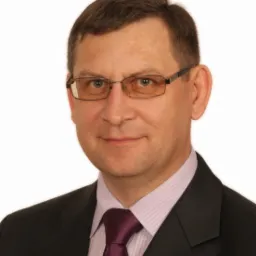 Portret mężczyzny w garniturze i okularach, z fioletowym krawatem, na jasnym tle. Profesjonalny wizerunek agenta ubezpieczeniowego.