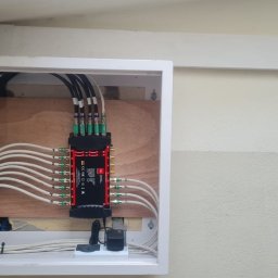 Firma Usługowo Handlowa Bąk Jacek - Rozdzielacz sygnału TV w skrzynce, z podłączonymi kablami koncentrycznymi. Widoczne złącza i przewody. Instalacja wewnątrz budynku.