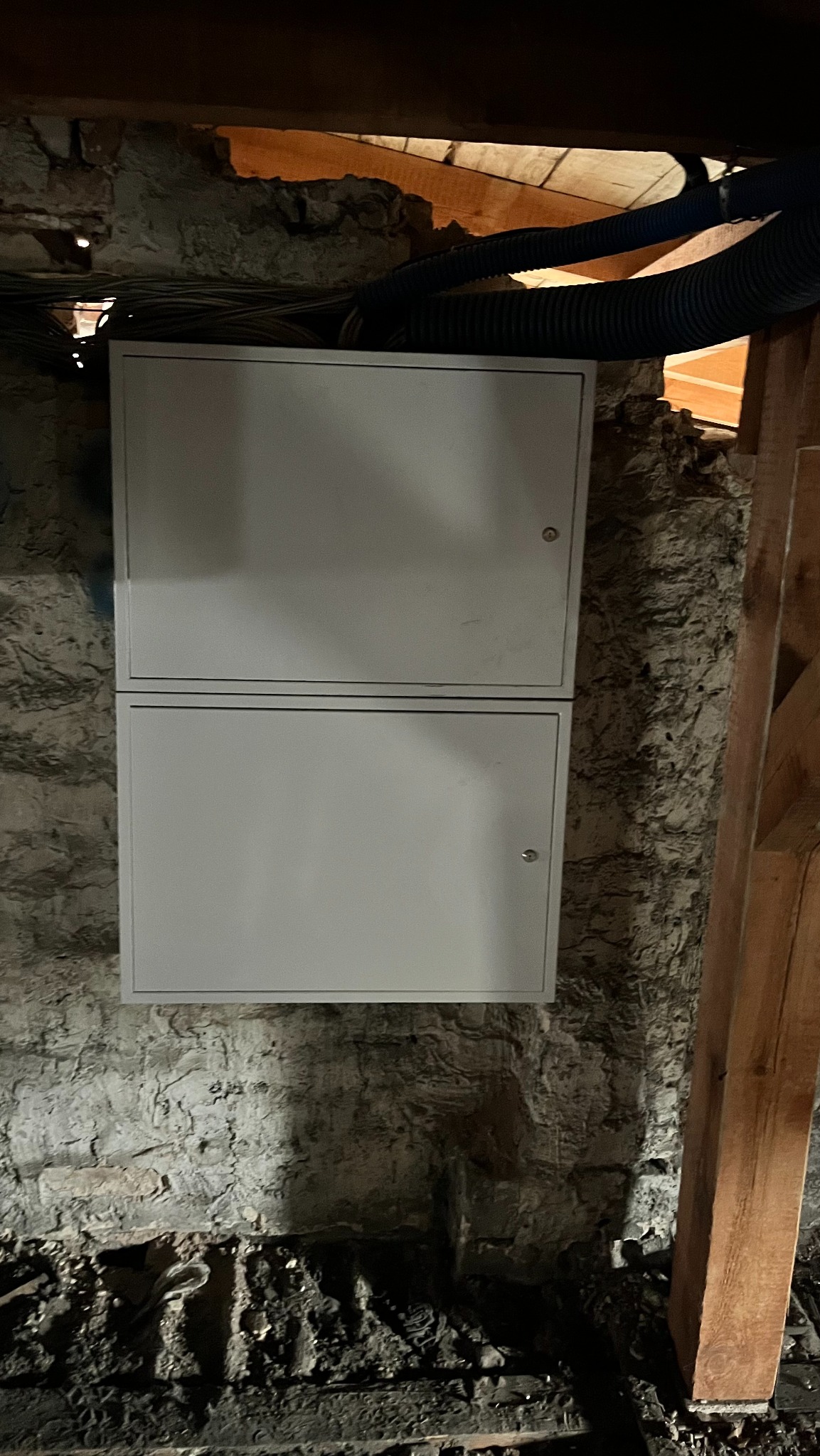 Dwu-segmentowa skrzynka telekomunikacyjna w surowym wnętrzu poddasza w Sosnowcu, z widocznymi przewodami i elementami konstrukcyjnymi.