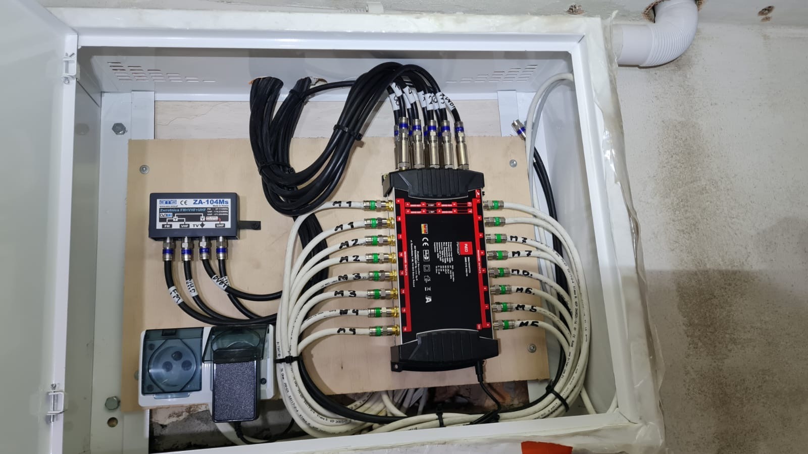Rozdzielacz antenowy ZA-104Ms i multiswitch z podłączonymi kablami koncentrycznymi w skrzynce instalacyjnej. Widoczne oznaczenia portów M1-M7.
