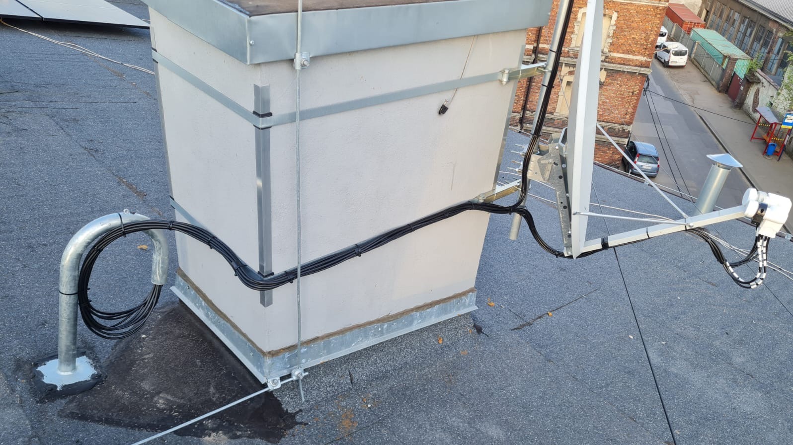 Antena satelitarna zamontowana na dachu budynku, z widocznymi kablami i elementami mocującymi. Instalacja wykonana schludnie, z dbałością o detale.
