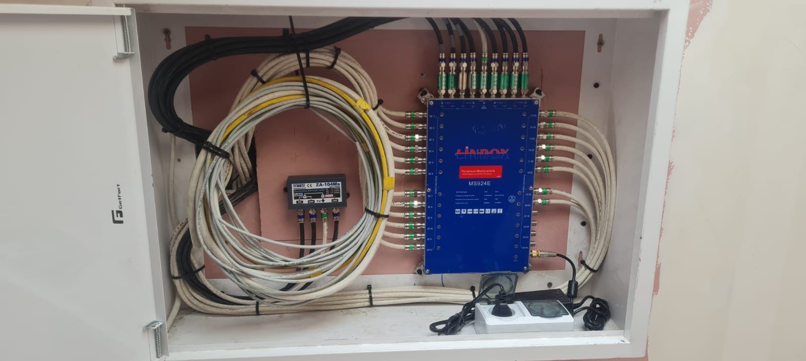 Rozdzielnica telekomunikacyjna Lindox MS924E z kablami koncentrycznymi i zasilaczem w białej obudowie. Widoczne złącza F i przewody.