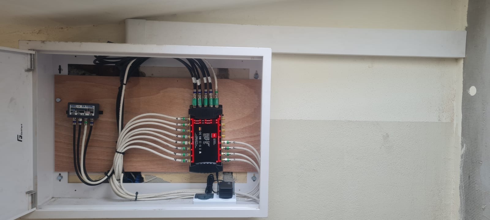 Rozdzielacz sygnału TV w skrzynce, z podłączonymi kablami koncentrycznymi. Widoczne złącza i przewody. Instalacja wewnątrz budynku.