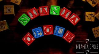 Napis 'Niania Opole' ułożony z kolorowych, drewnianych klocków na ciemnym drewnianym tle, otoczony innymi klockami z literami i obrazkami.