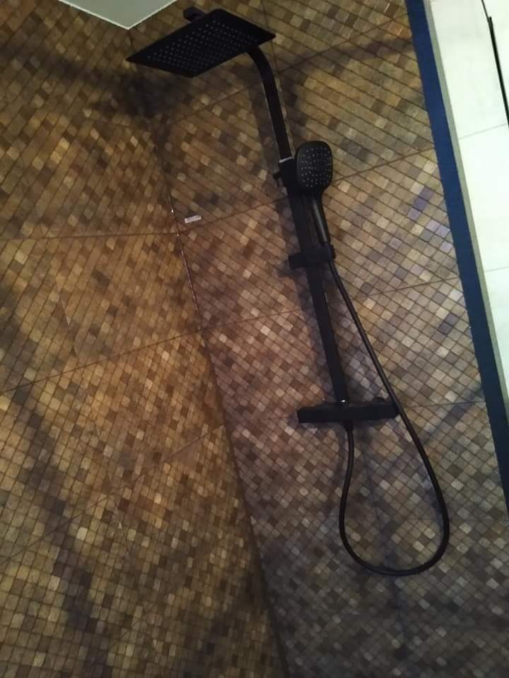 Czarny zestaw prysznicowy z deszczownicą i słuchawką na mozaikowej ścianie w łazience.