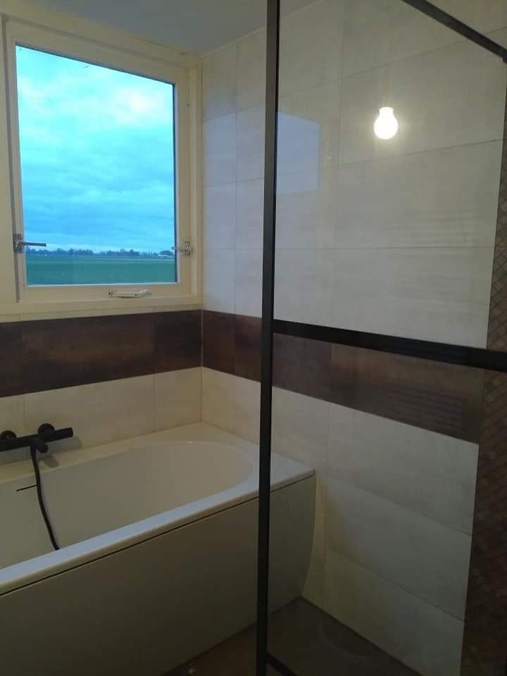 Wykończona łazienka w Białymstoku z wanną, biało-brązowymi płytkami i widokiem na krajobraz za oknem.