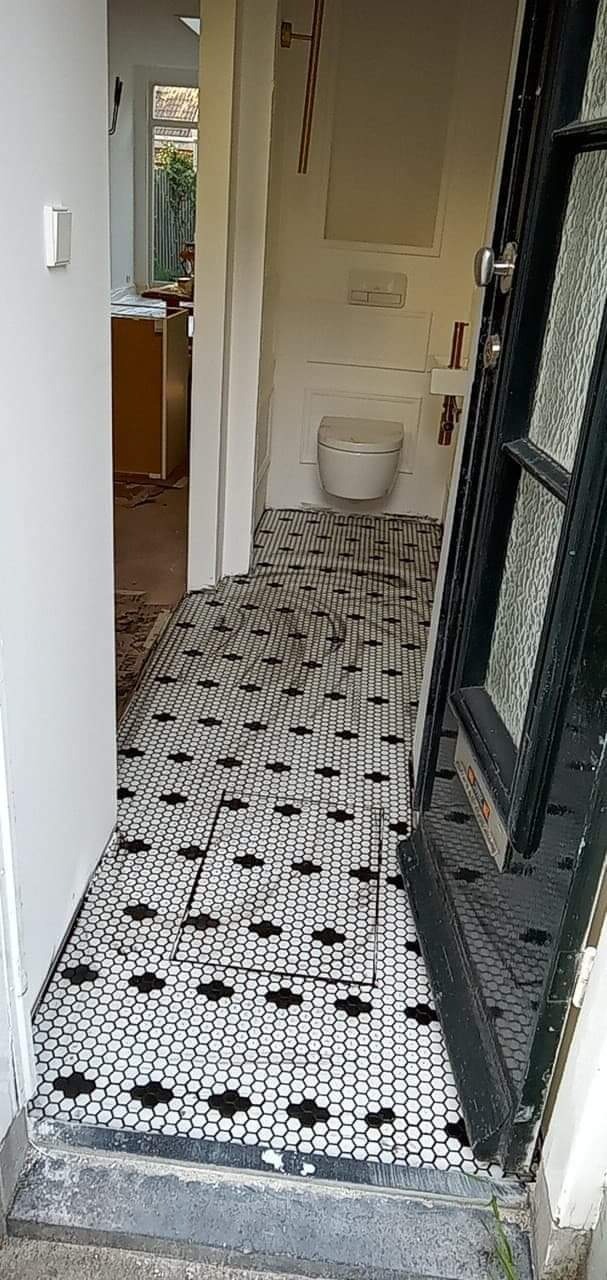 Ułożona czarno-biała mozaika podłogowa z heksagonów w przedpokoju i łazience, widoczny fragment otwartych drzwi wejściowych i toaleta w tle.