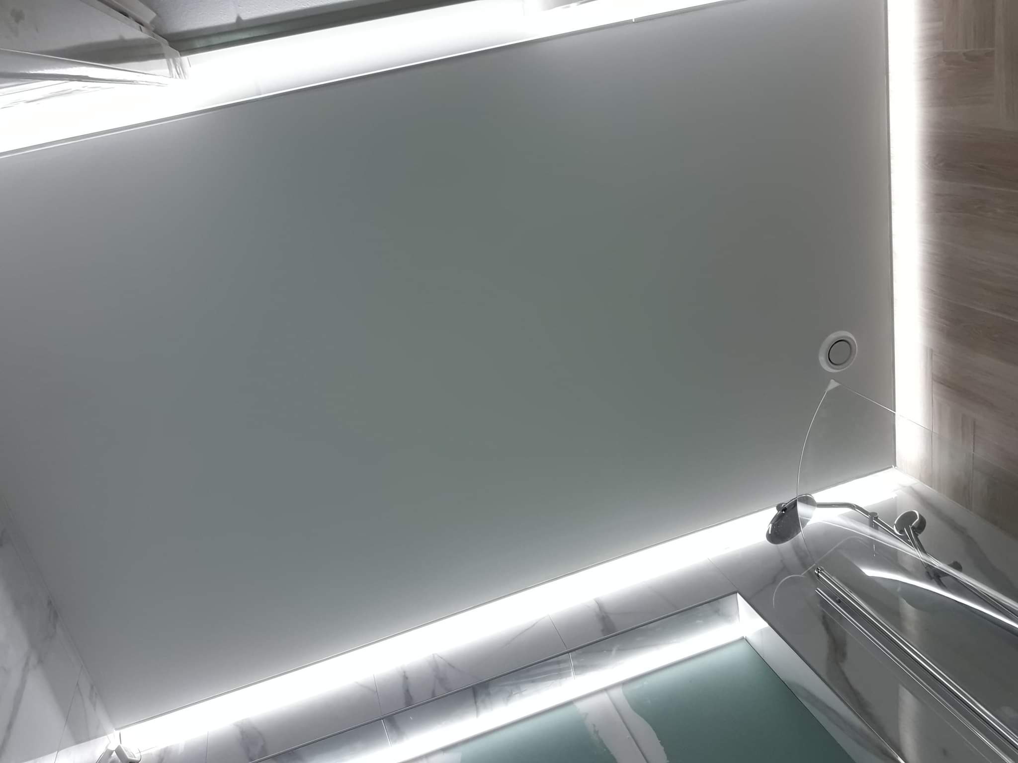 Nowoczesny sufit napinany w łazience z oświetleniem LED, widoczna kabina prysznicowa i marmurowe płytki na ścianach.