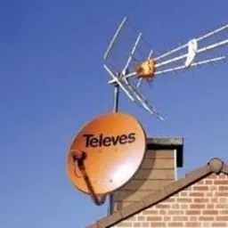 Antena satelitarna Televes w kolorze pomarańczowym zamontowana na kominie z cegły, na tle błękitnego nieba. Widoczna również antena naziemna.