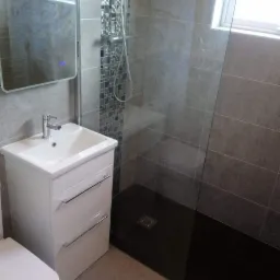 Nowoczesna łazienka z kabiną prysznicową typu walk-in, mozaiką na ścianie przy prysznicu, białą szafką z umywalką i czarnym brodzikiem.