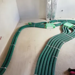 Rozprowadzenie rur wentylacyjnych, zielone karbowane przewody z czerwonymi końcówkami, połączone w skrzynki na podłodze w surowym wnętrzu.