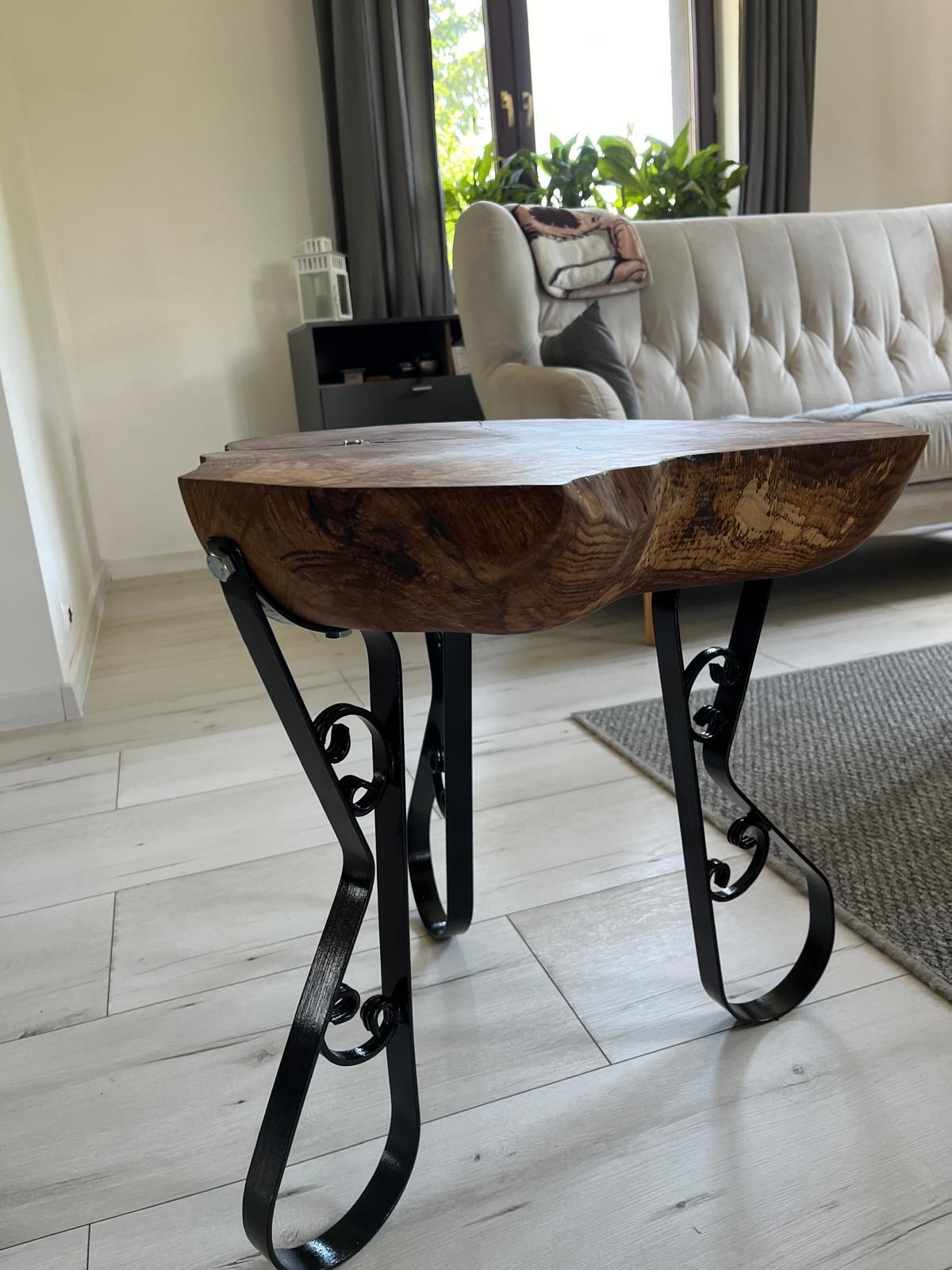 Stolik kawowy z blatem z surowego drewna i dekoracyjnymi metalowymi nogami w stylu retro, widoczny w jasnym salonie z sofą i dywanem.