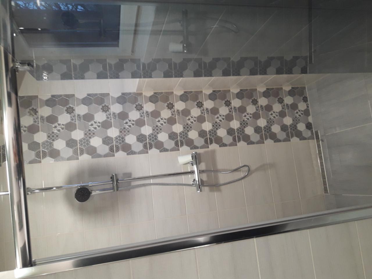 Wykończona kabina prysznicowa z chromowaną armaturą i dekoracyjnymi, heksagonalnymi płytkami w odcieniach szarości, oddzielona szklaną ścianką.