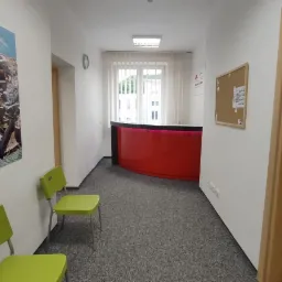 Wnętrze szkoły językowej: korytarz z recepcją, plakat z widokiem na Peniscolę i zielone krzesła dla oczekujących.