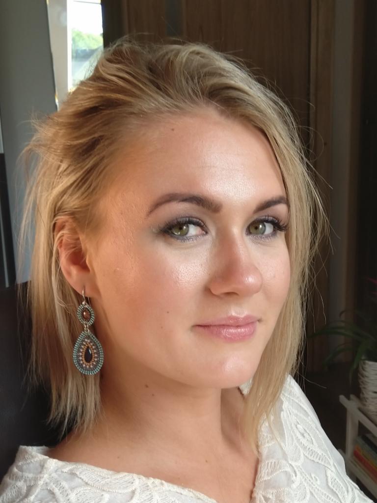 Portret blondynki z delikatnym makijażem, na sobie ma białą bluzkę z koronką i ozdobne kolczyki.