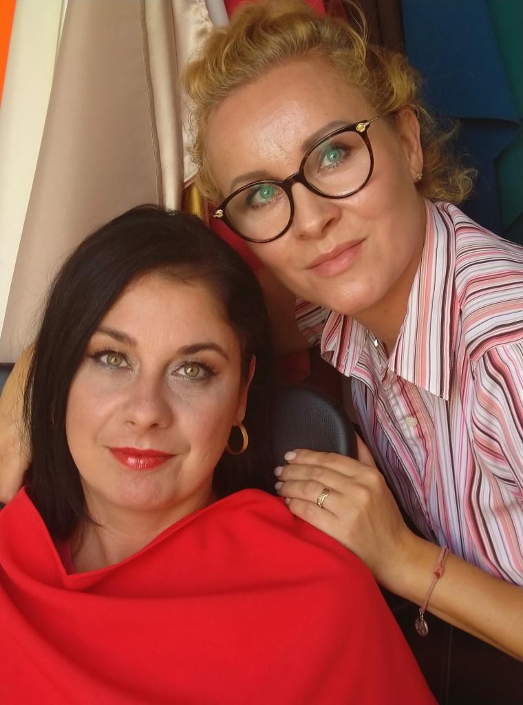 Portret dwóch kobiet: brunetki z czerwonym szalem i blondynki w okularach, uśmiechnięte, z delikatnym makijażem, w naturalnym świetle.